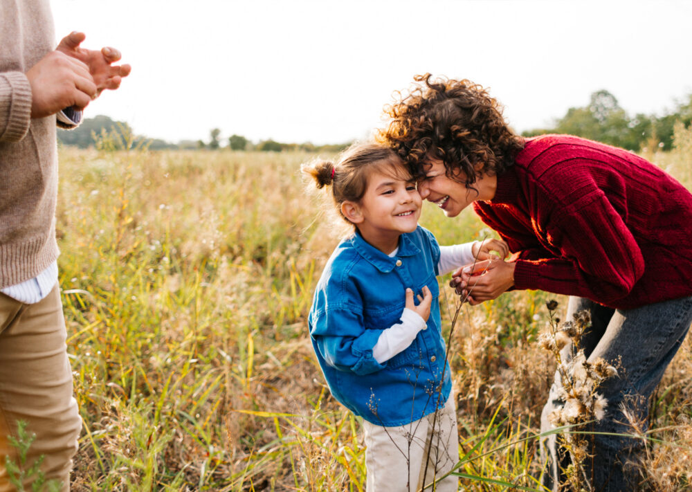 Woman leaning down to little girl both laughing in tall field | Master-Planned Community in McKinney