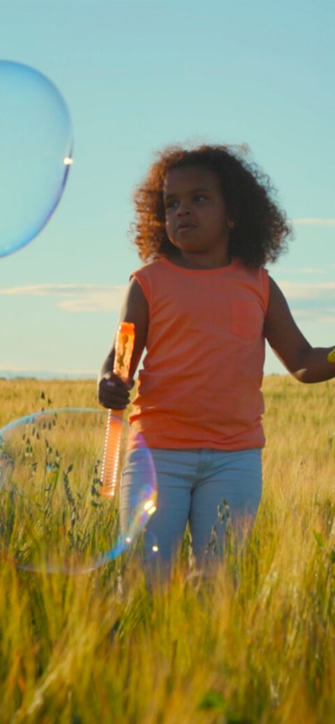 Child blowing large bubbles in a golden field | Master-Planned Community in McKinney